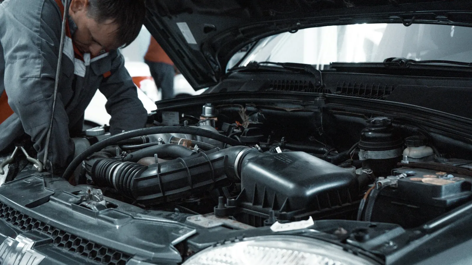 Mechanik v pracovním oděvu kontroluje motor auta s otevřenou kapotou
