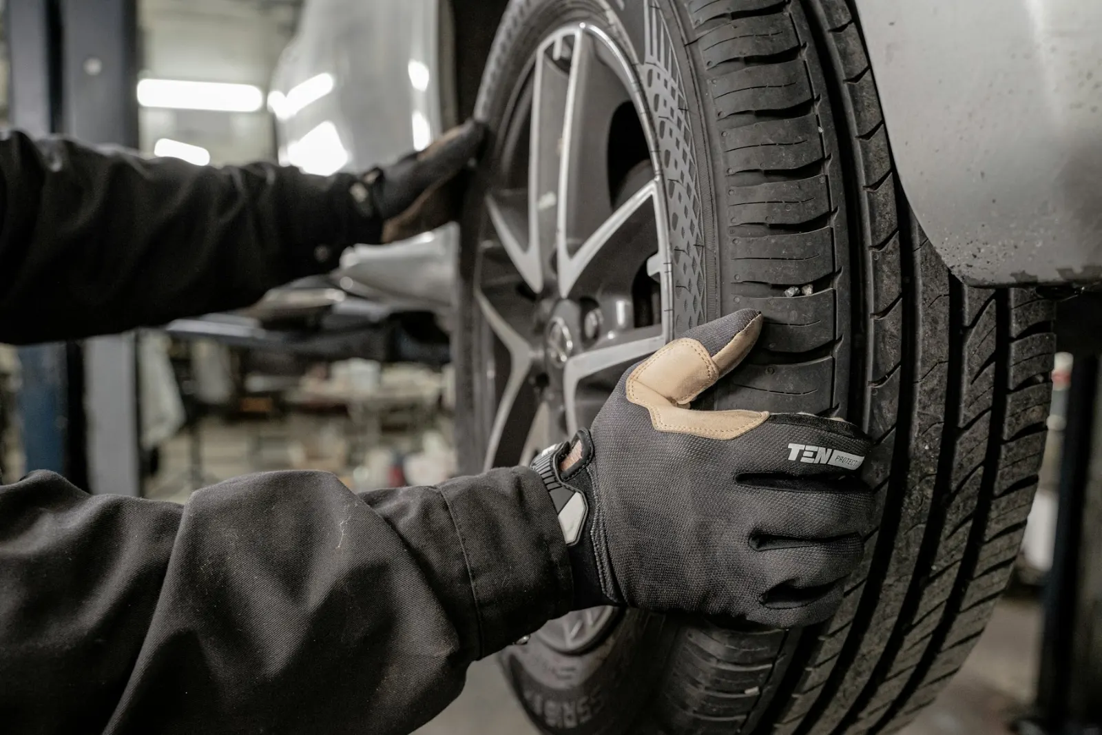 Mechanik v rukavicích kontroluje vzorek pneumatiky na kole vozu na zvedáku